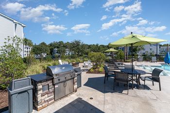 a patio with a grill and tables with umbrellas and a swimming pool at The Parker Myrtle Beach, Myrtle Beach, SC